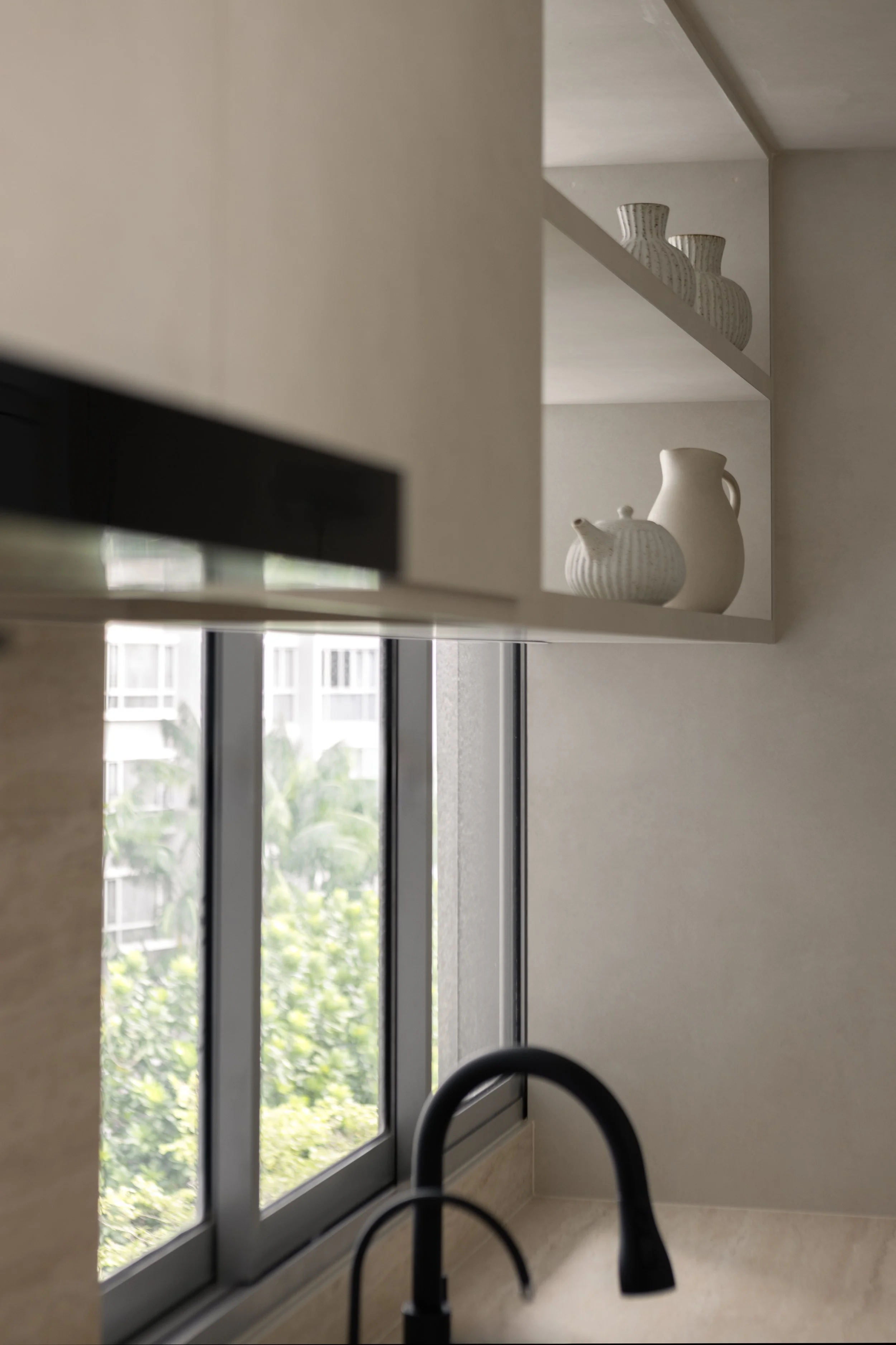 Part of a kitchen with a window, black sink faucet, and open shelves holding white ceramic vases.
