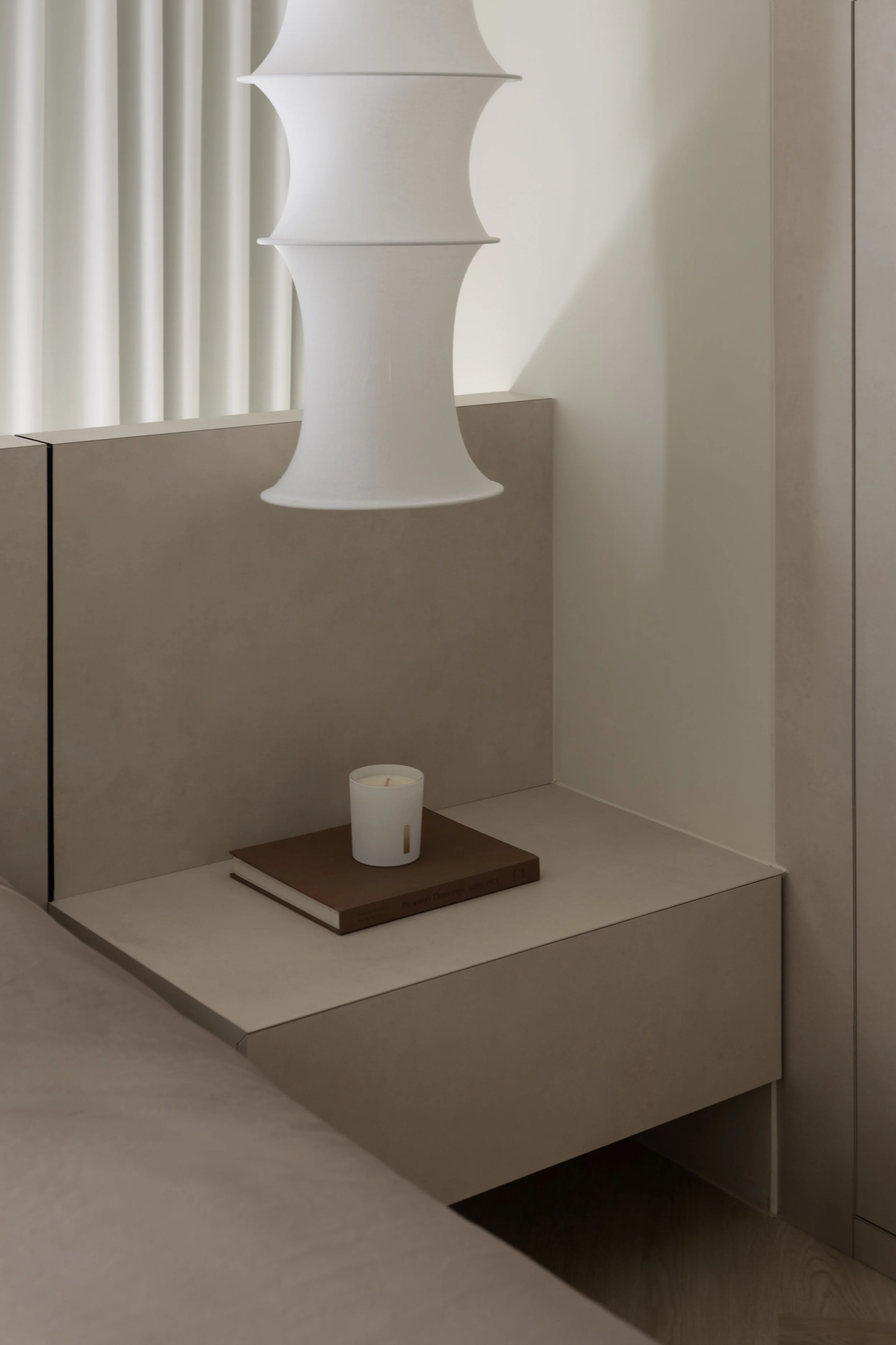 Minimalist bedroom nightstand with a white candle, a book, and a white sculptural hanging lamp.