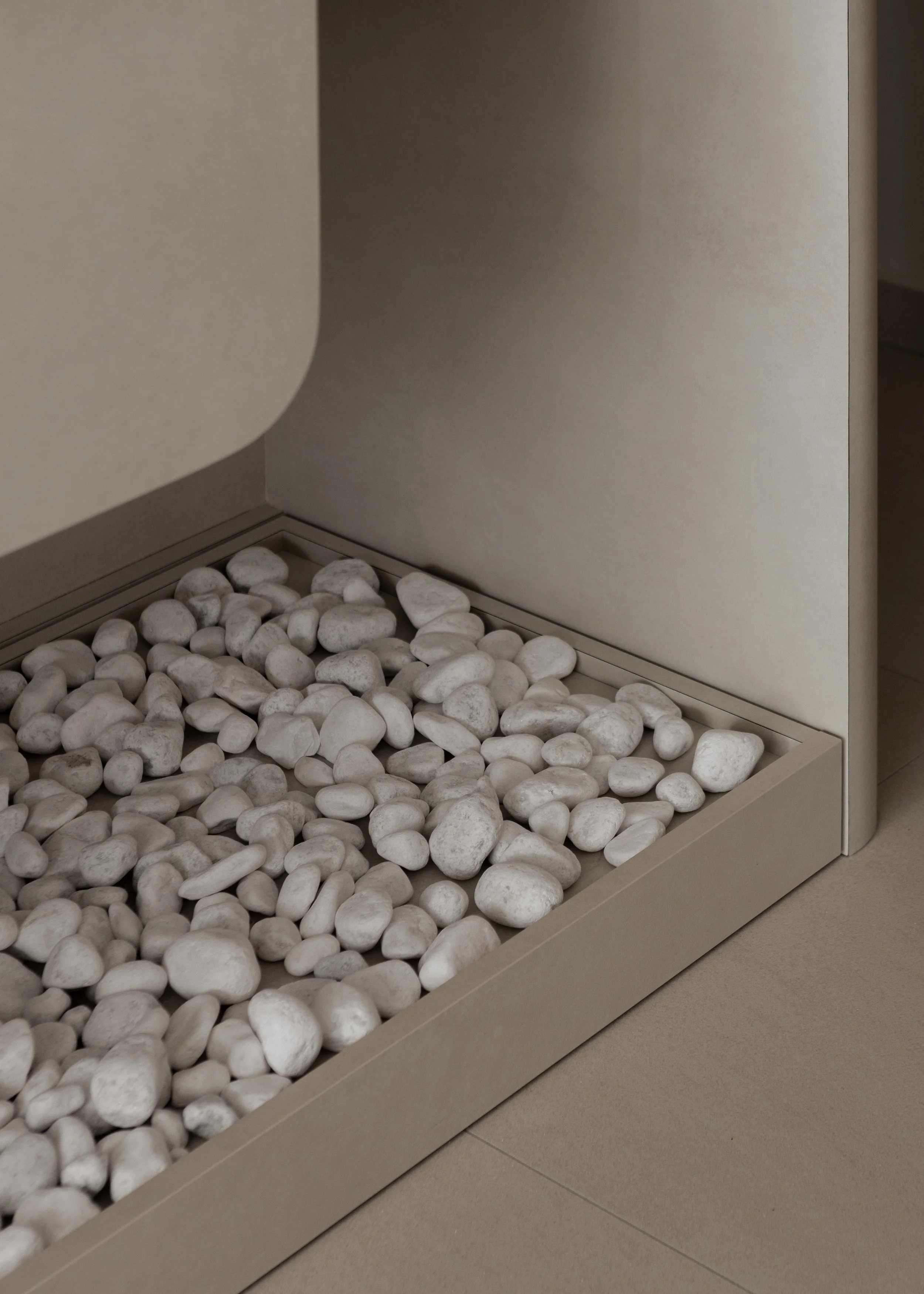 Close-up of a modern beige cabinet with a decorative pebble tray at its base, featuring white smooth stones, on a beige tiled floor.