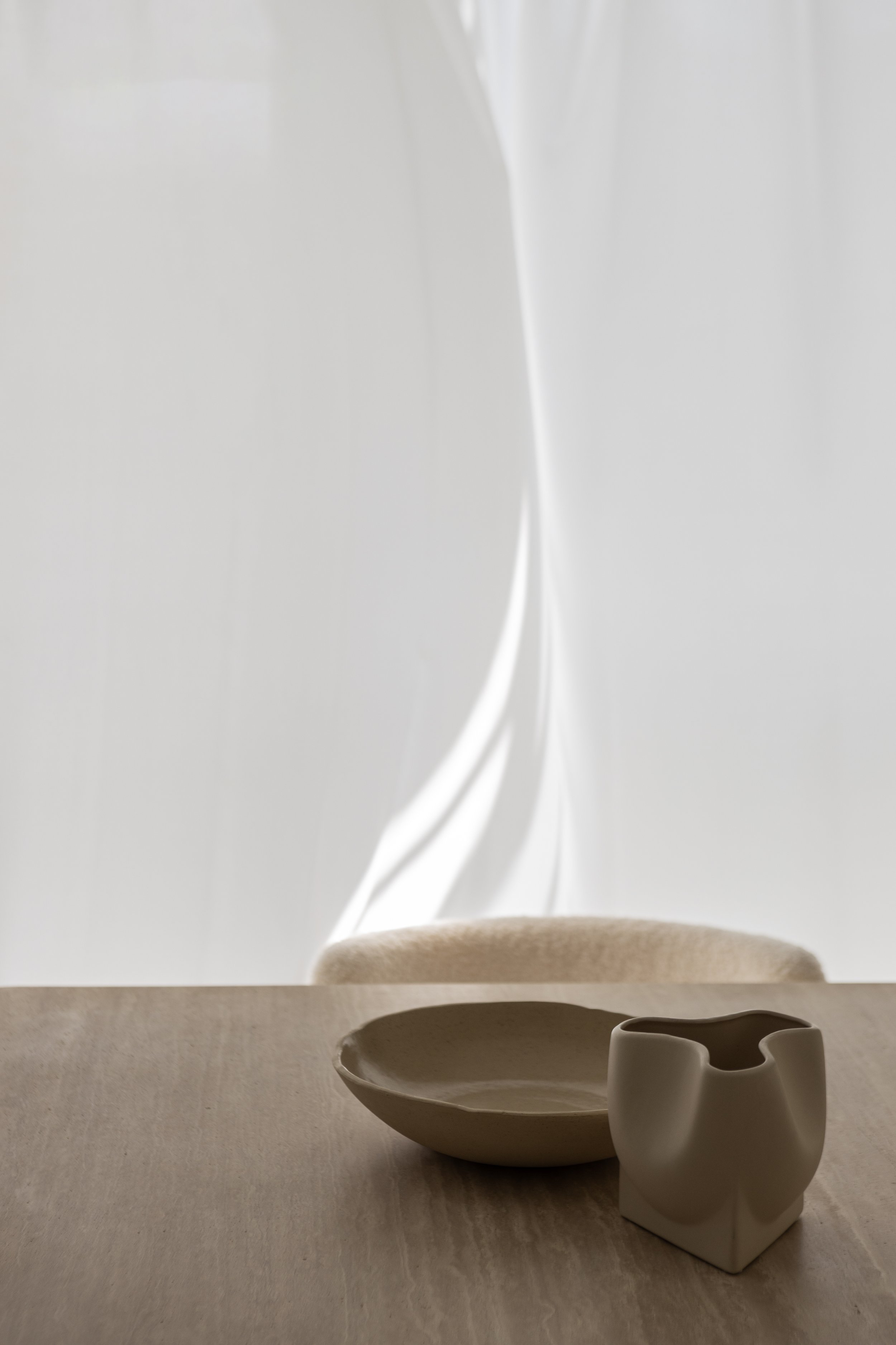 A minimalist ceramic bowl and vase on a wooden table with a soft, abstract background.
