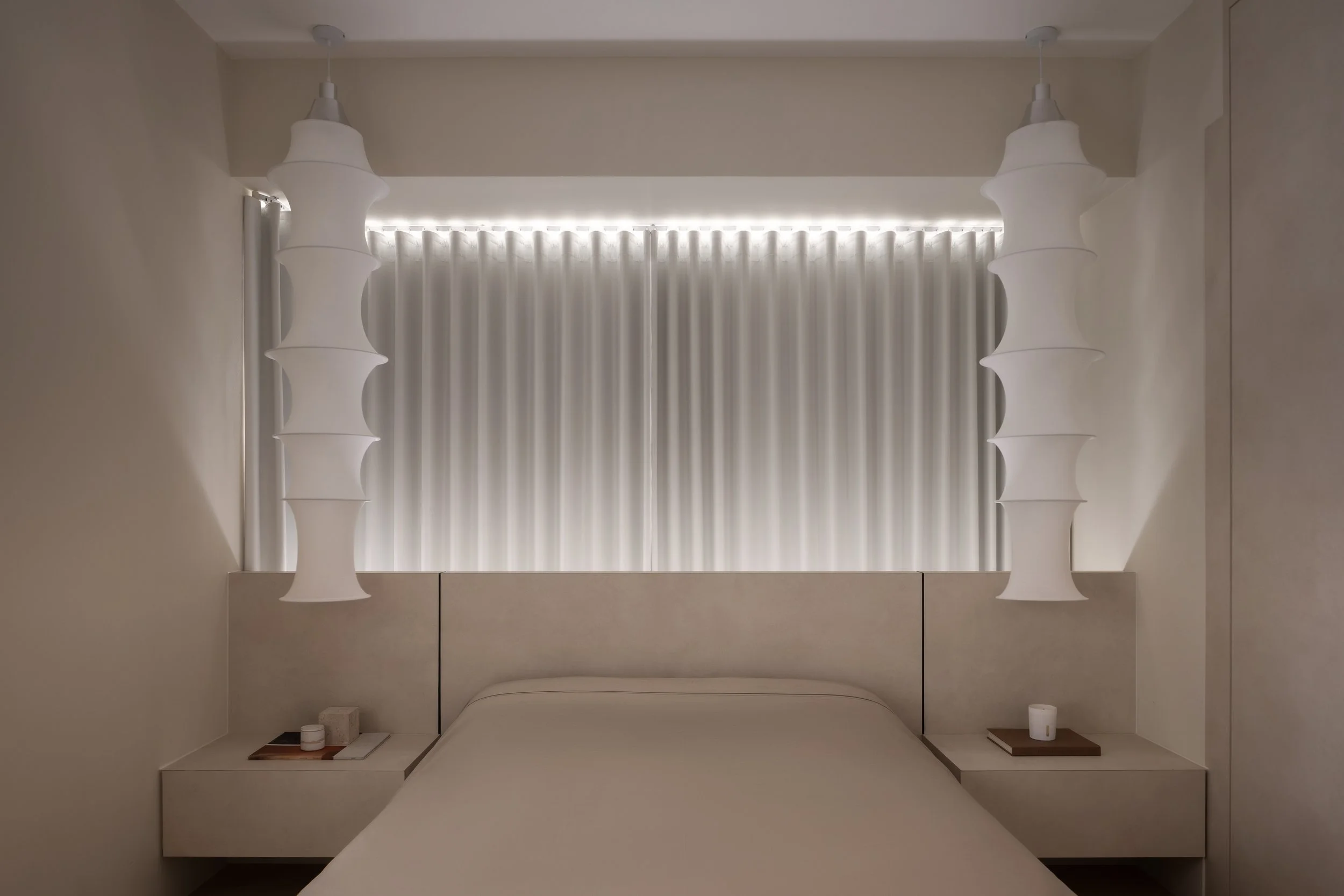 Minimalist bedroom with a white bed, beige headboard, two hanging pendant lights, and a window with vertical blinds.