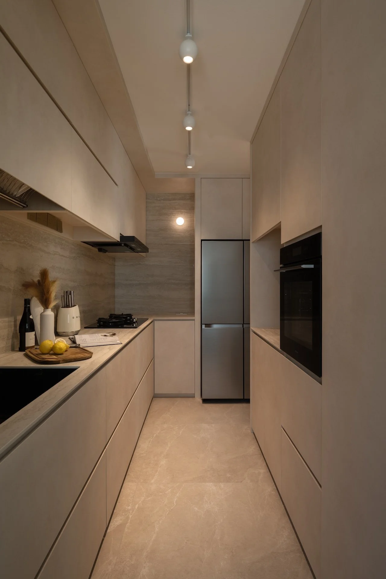 Modern kitchen with beige cabinets, marble countertops, stainless steel refrigerator, built-in oven, and minimal lighting.