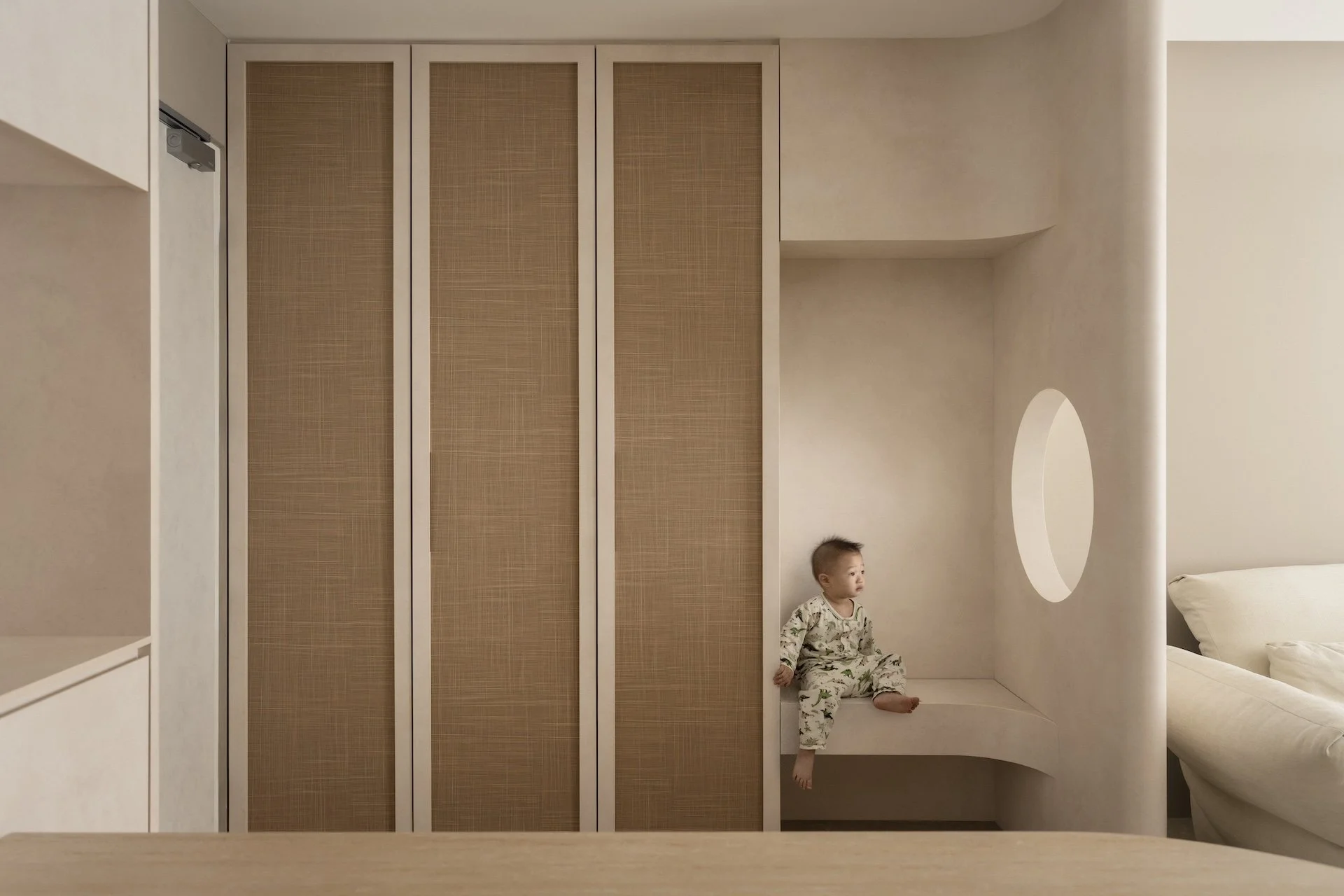 Child sitting on built-in seating area next to a small circular window in a modern minimalist room.