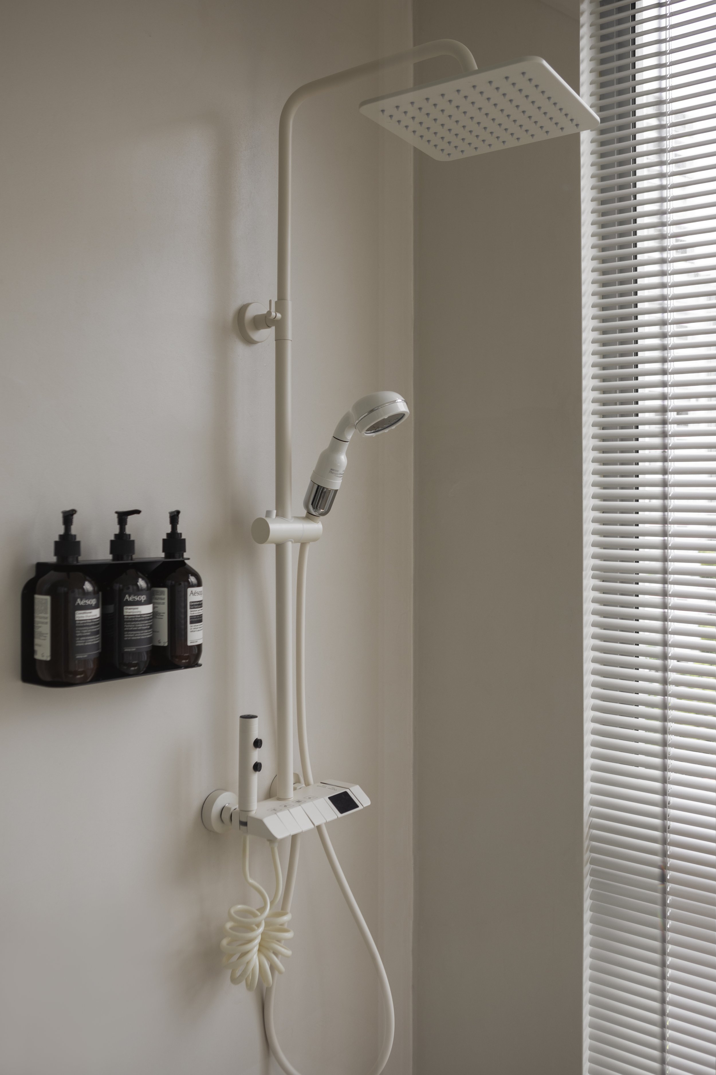 Shower with overhead rain showerhead, handheld showerhead, soap dispensers, and window with blinds.