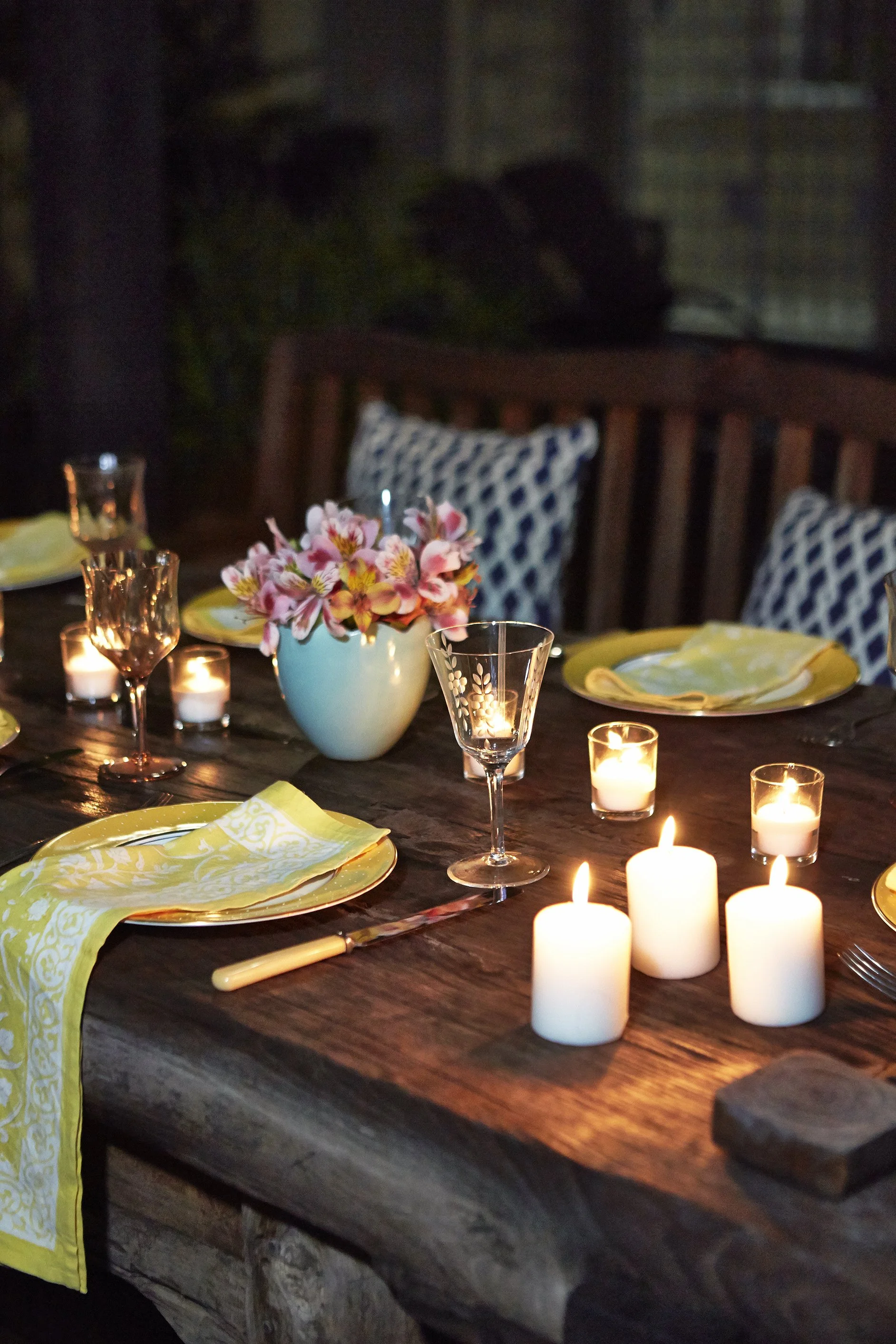 A wooden table with candles, plateware, and glasses on top.