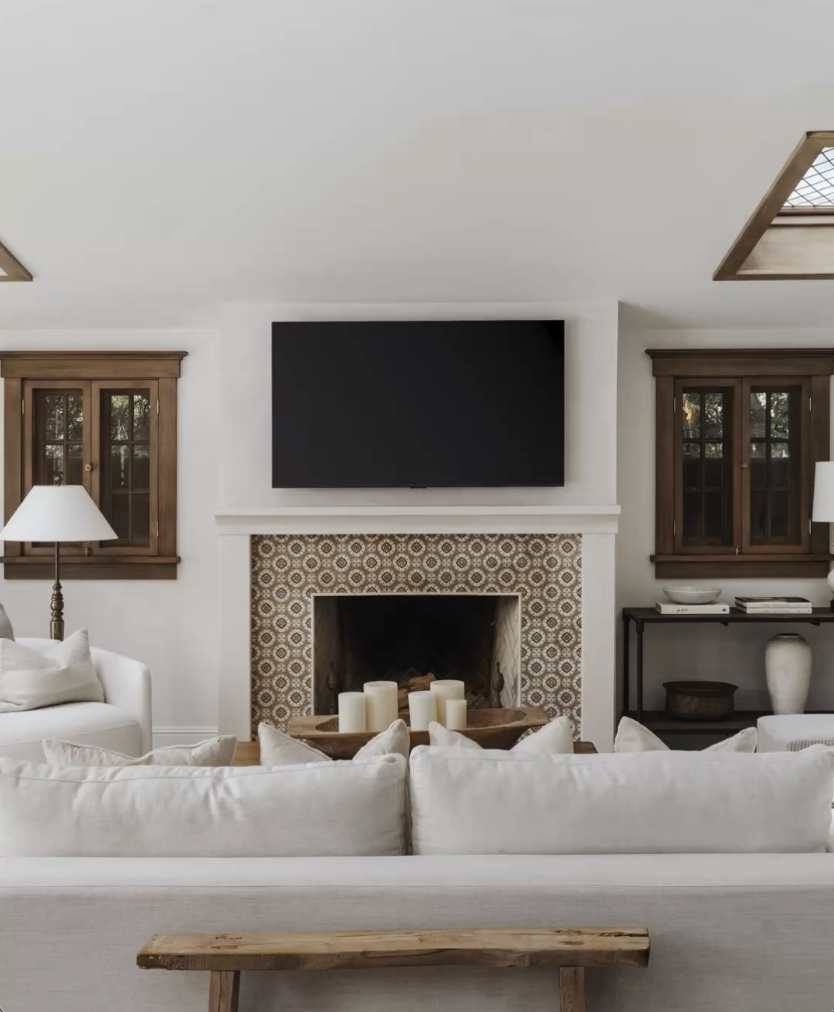 Living room with a white couch, a fireplace with candles, a mounted TV, two wooden cabinets, and two windows.