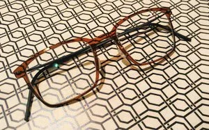 A pair of eyeglasses with brown and black frames resting on a geometric patterned surface.