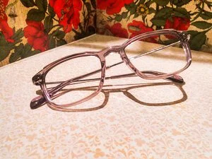 A pair of clear eyeglasses resting on a surface with a floral-patterned background.