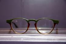 Green and brown eyeglasses resting on a metallic surface.