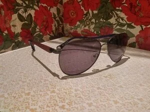 Pair of sunglasses with dark tinted lenses resting on a textured surface, with a floral patterned background.