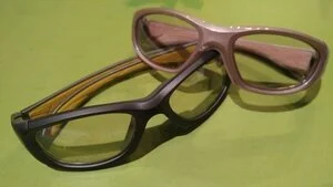 Two pairs of eyeglasses, one with a brown frame and the other with a black and yellow striped frame, placed on a green surface.