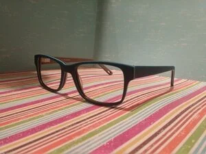 Black rectangular eyeglasses on a colorful striped surface with a plain background