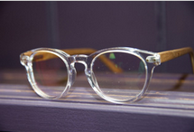 Clear eyeglasses with round lenses and wooden temples resting on a wooden surface.