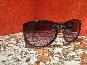 A pair of large black sunglasses with dark lenses resting on a floral patterned surface with a red wall in the background.
