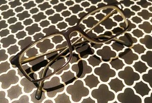 A pair of black glasses resting on a black and white trellis patterned surface.