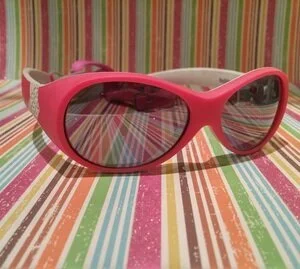 Pink children's sunglasses with dark lenses on a colorful striped surface.
