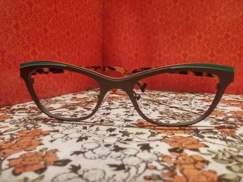 Pair of eyeglasses with black and tortoise shell frames on a floral-patterned tablecloth.