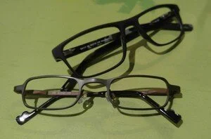 Two pairs of eyeglasses, one black and one metallic, placed on a green surface.