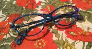 Pair of eyeglasses with black, blue, and red frames on a floral tablecloth.