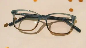 A pair of eyeglasses with dark frames lying on a white surface with small brown dots.
