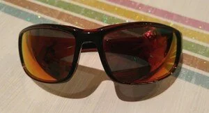 Pair of sunglasses with black frame and orange-tinted lenses on a striped surface.