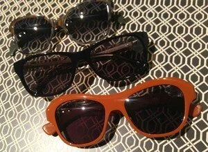 Three pairs of sunglasses on patterned background, two black and one orange.
