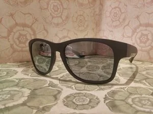 Pair of black sunglasses with tinted lenses resting on a patterned surface.
