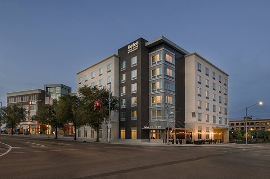 A modern multi-story building at an intersection with trees and streetlights during dusk.