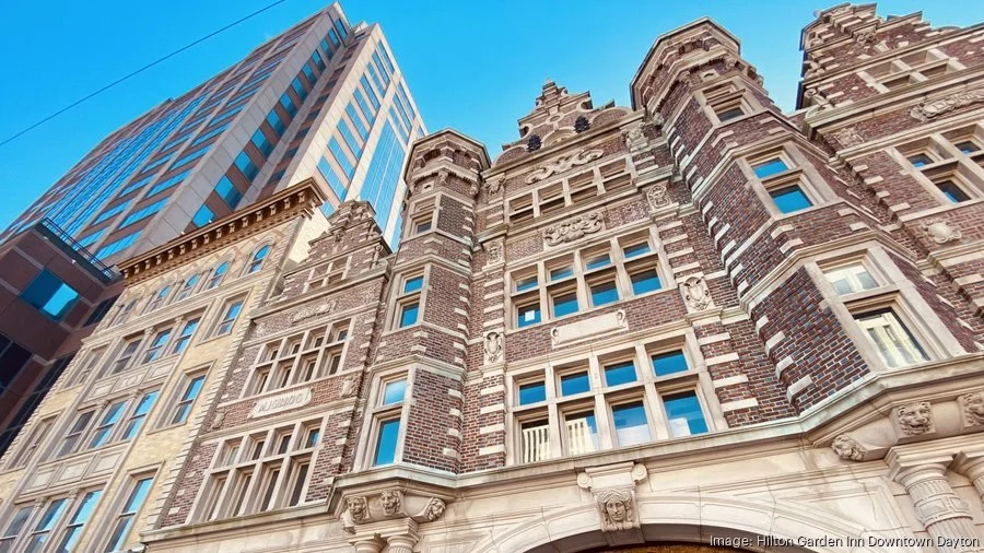 Low-angle view of historic brick and stone building with ornate architectural details next to modern glass skyscraper against blue sky.