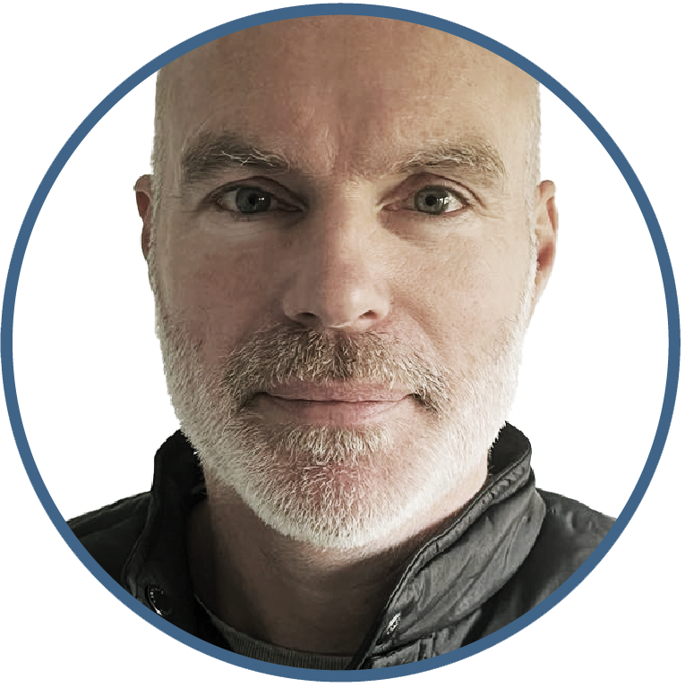 Close-up portrait of a middle-aged man with a bald head, gray beard, and mustache, wearing a black jacket, against a white background.