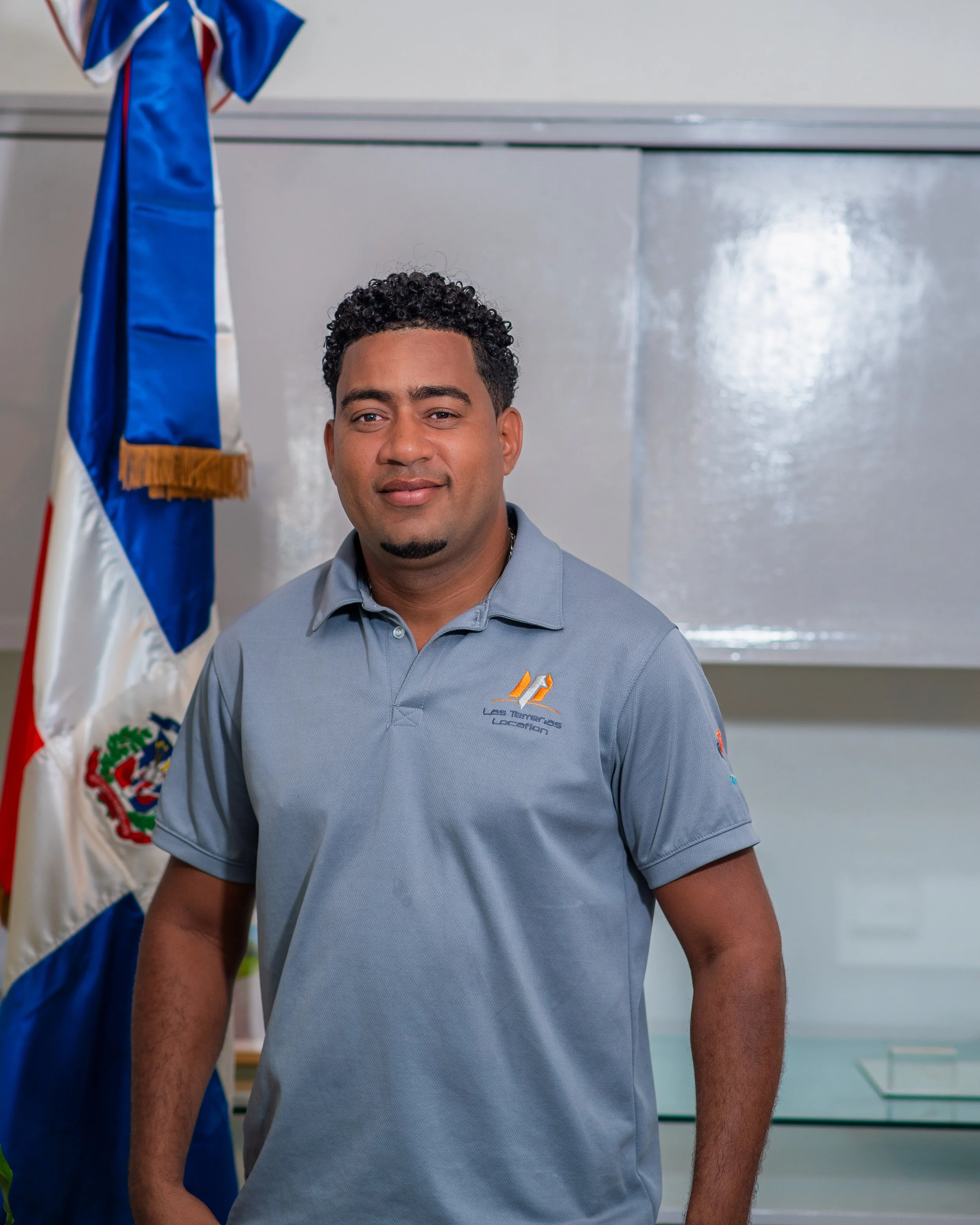 Hombre con camiseta gris frente a bandera dominicana.