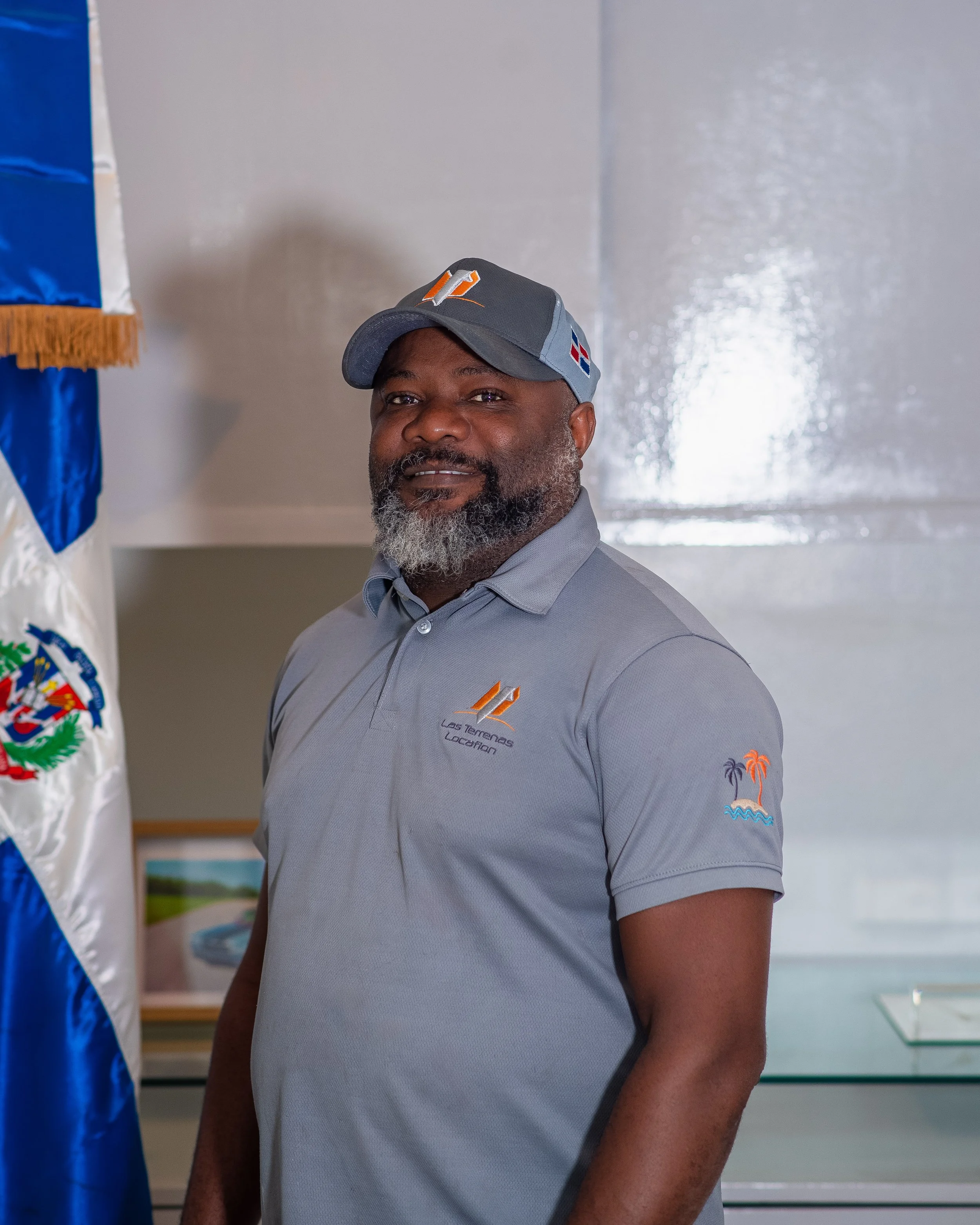 Hombre con gorra y camiseta gris con logos y palabras en un entorno interior.