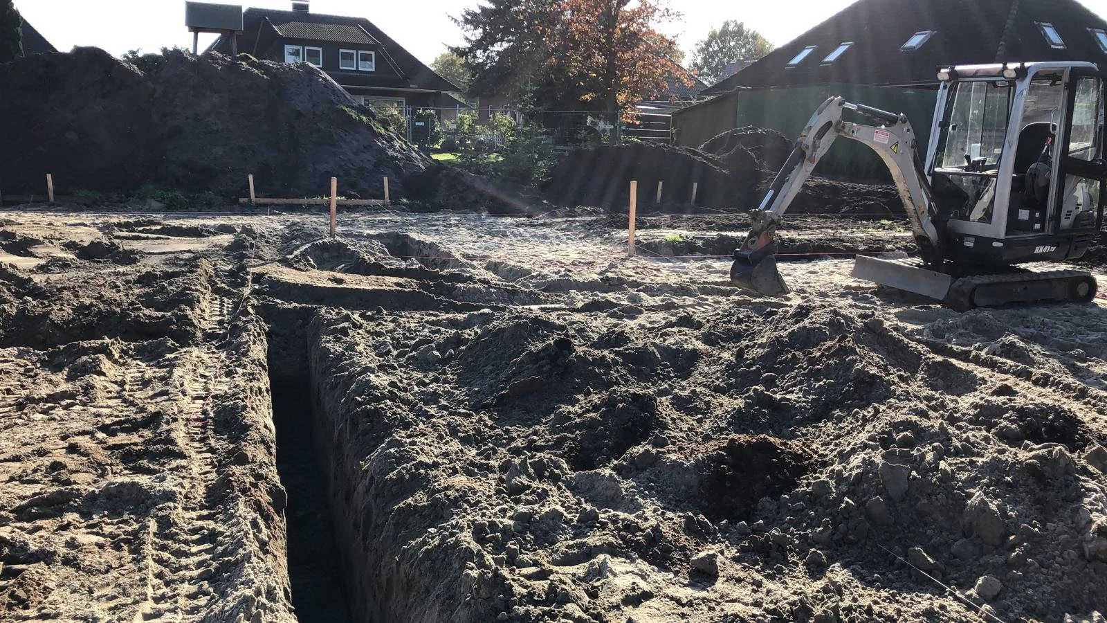 Baustelle mit Bagger, ausgegrabene Gräben und Baugrund in einem Vorort, Häuser im Hintergrund.