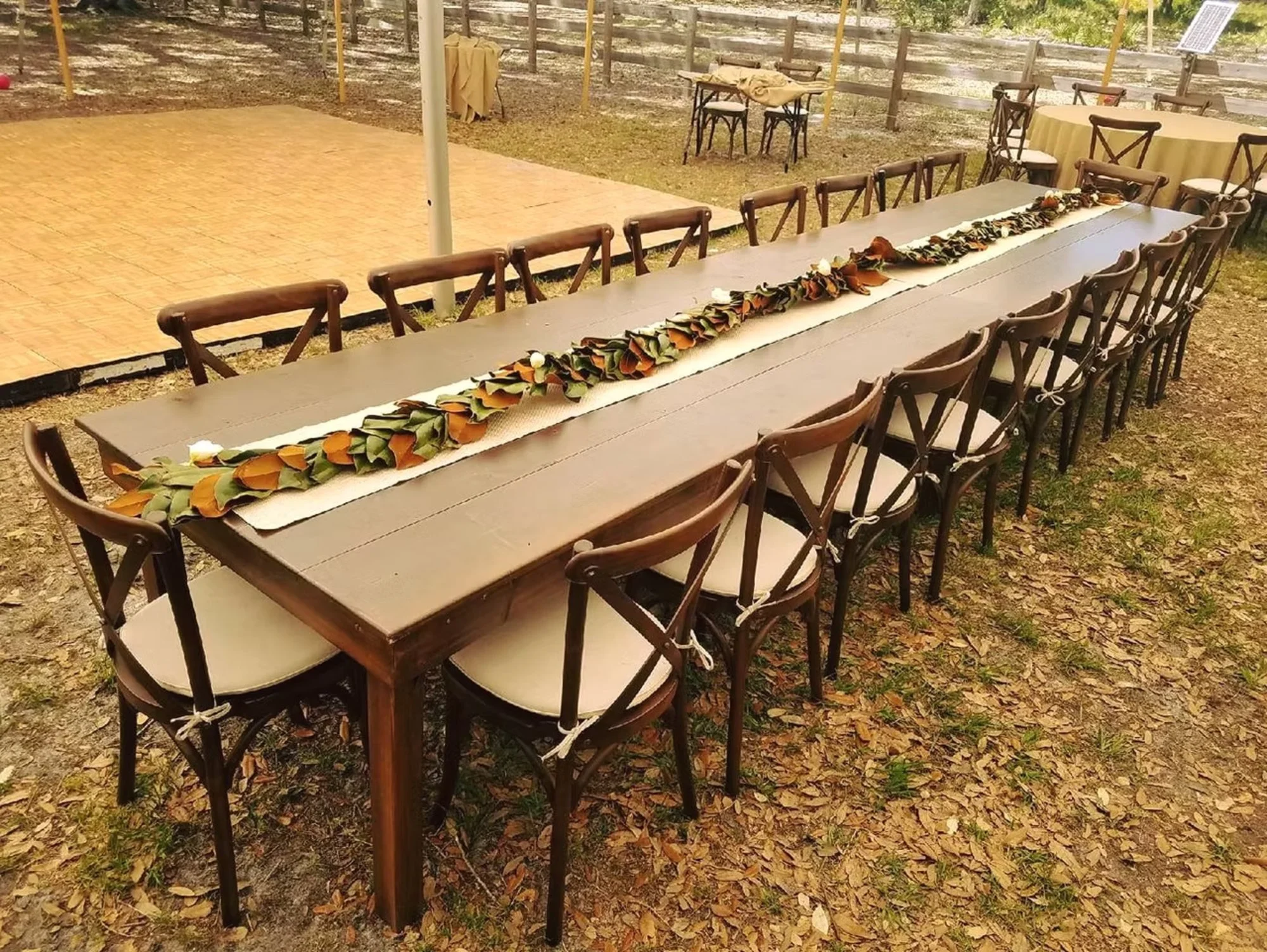 Long wooden dining table with chairs set up outdoors, decorated with a leafy garland.
