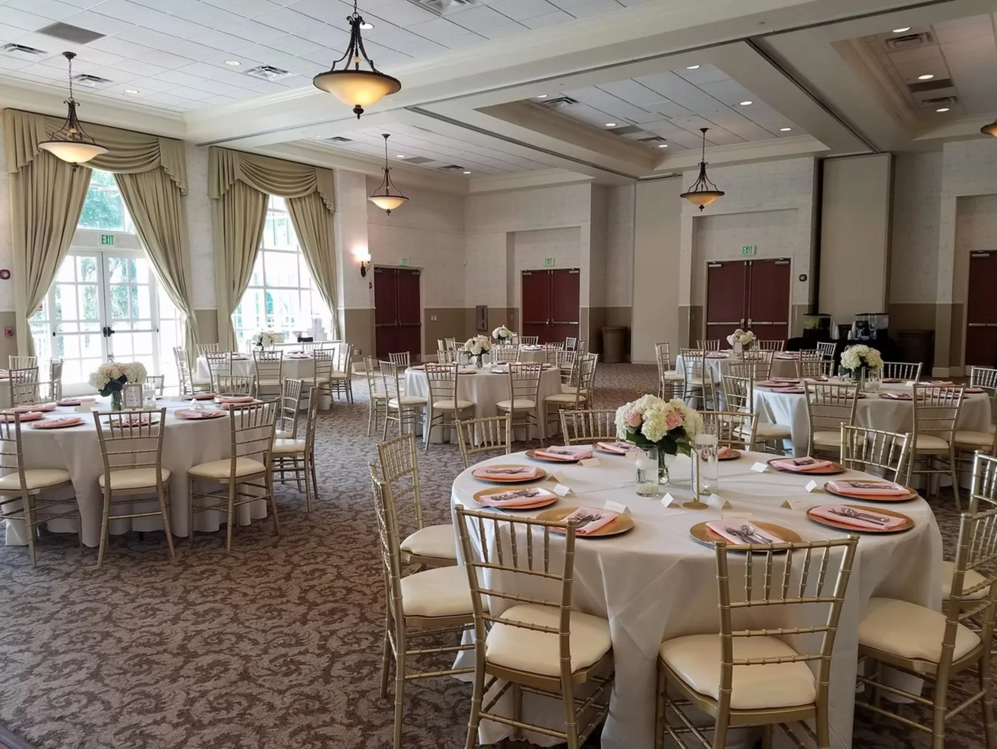 Elegant banquet hall with round tables set for an event, featuring white tablecloths, floral centerpieces, and gold chairs.