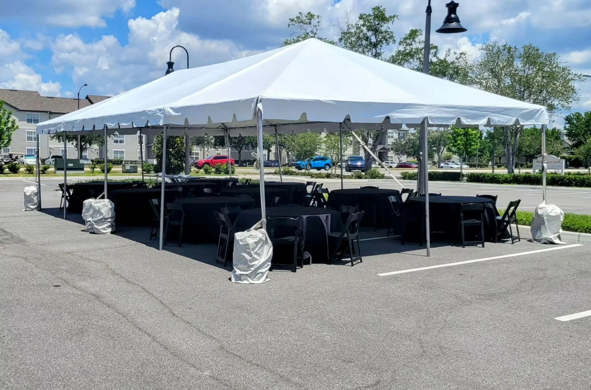 Outdoor event tent with black tables and chairs set up in a parking lot.