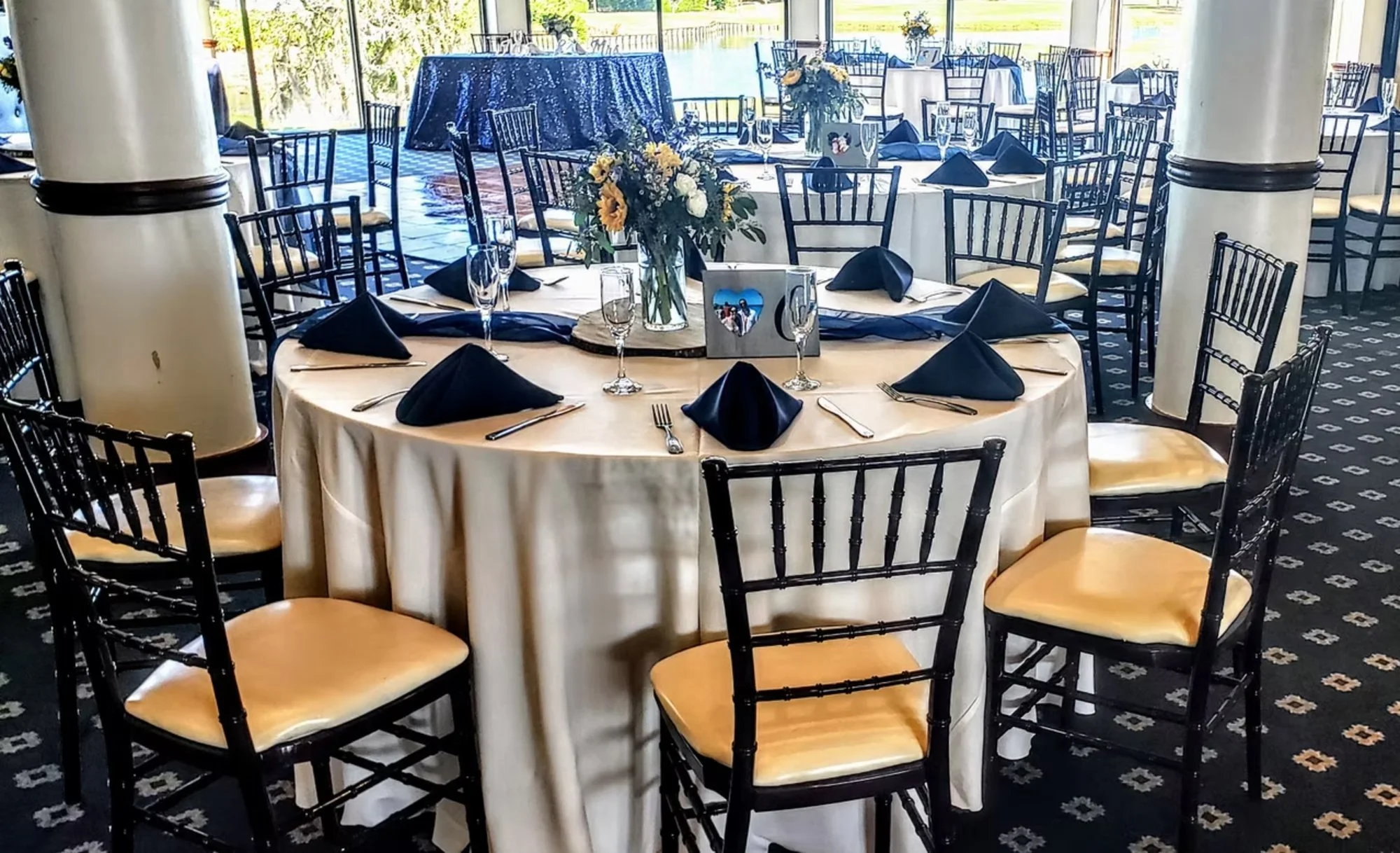 Elegant banquet hall with round tables, black chairs, floral centerpiece, and black napkins on white tablecloths.