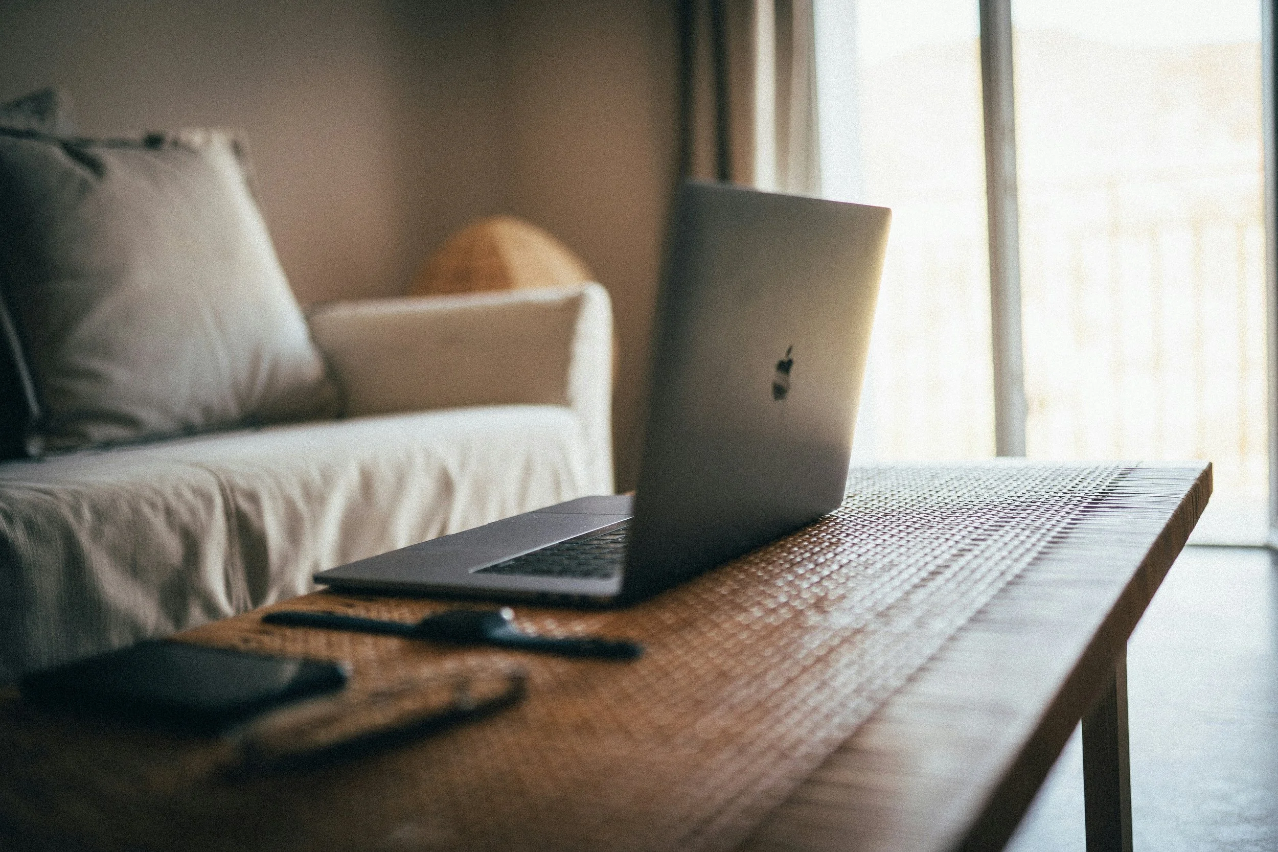 Laptop, remote, and mouse on a wooden table near a window.