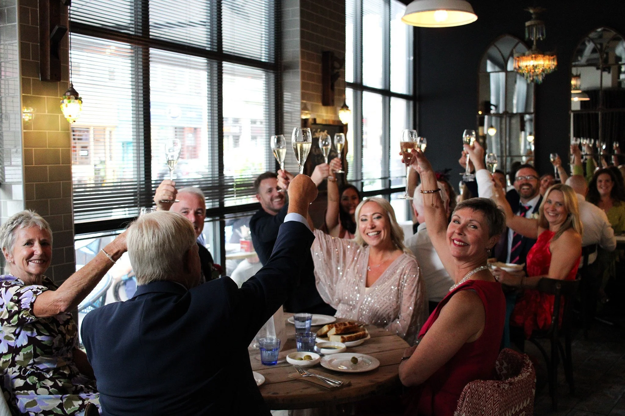 People celebrating with champagne at a restaurant, raising glasses in a toast, smiling and enjoying a festive gathering.