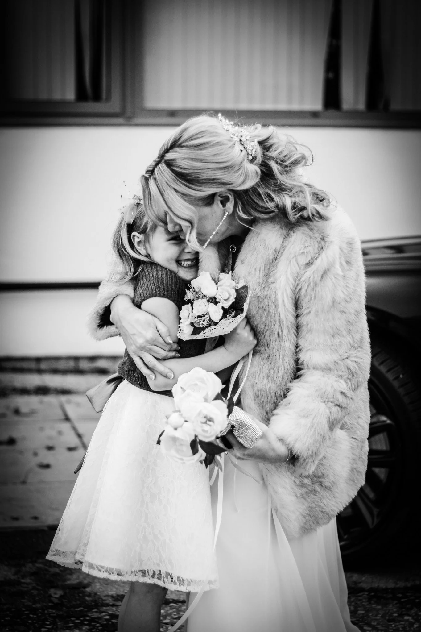 A woman and a young girl hugging, with the woman holding a bouquet of flowers. The scene appears joyful, possibly a wedding or special event.