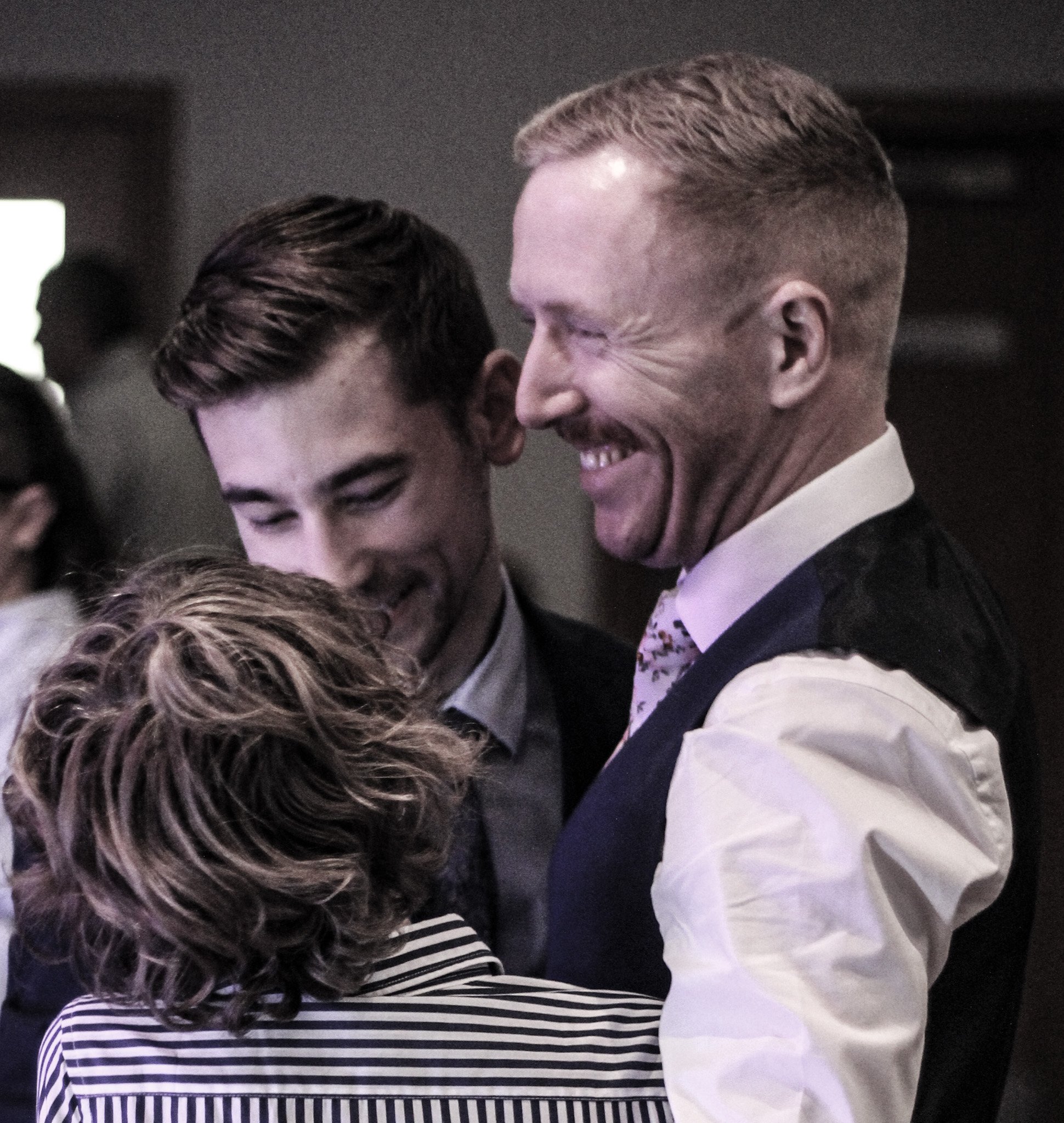 Three people engaged in conversation, smiling and laughing, at a social gathering.