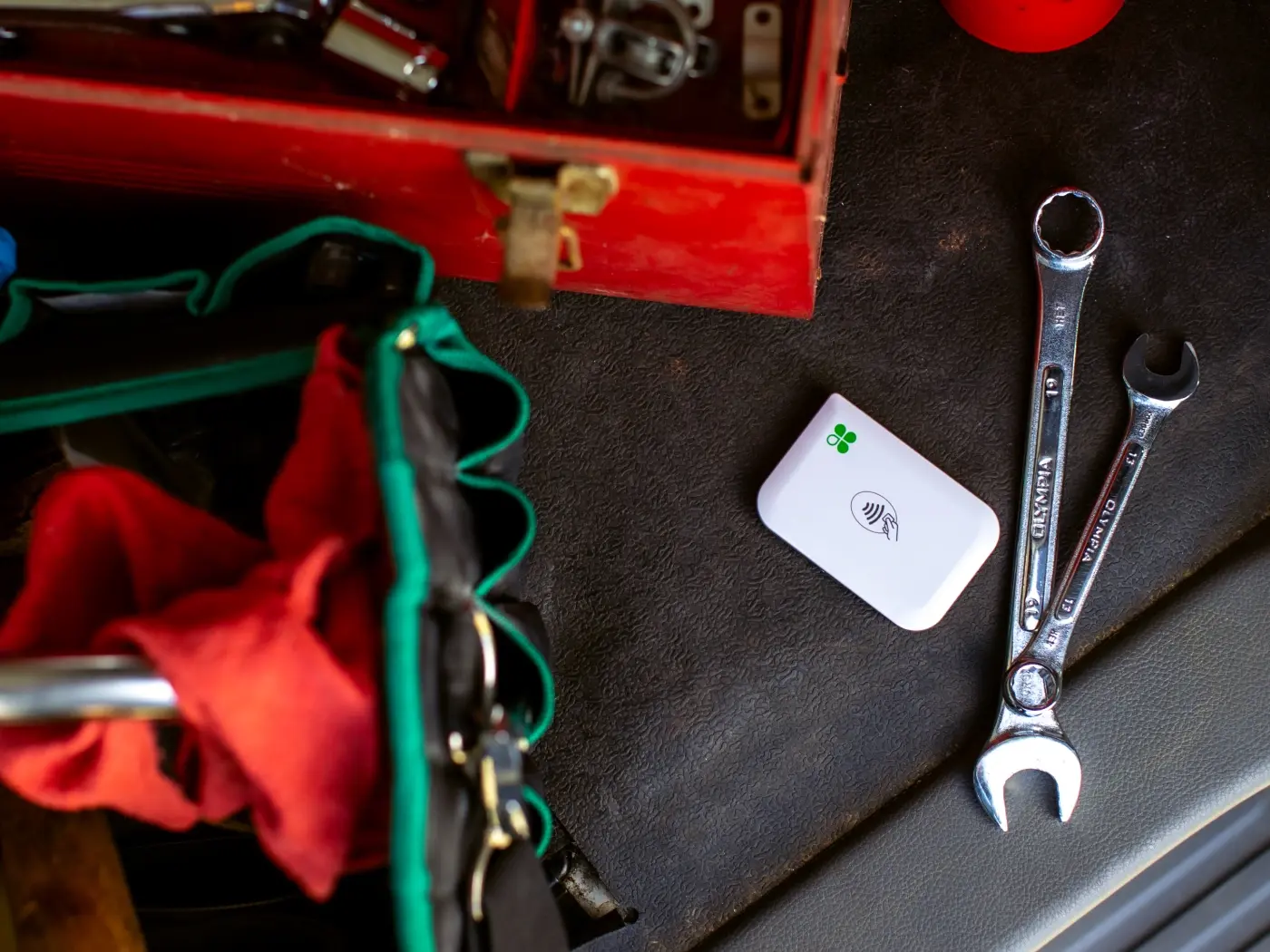 Automotive repair tools and supplies on a black surface, including a red toolbox, two wrenches, a white electronic device, and a multicolored cloth.