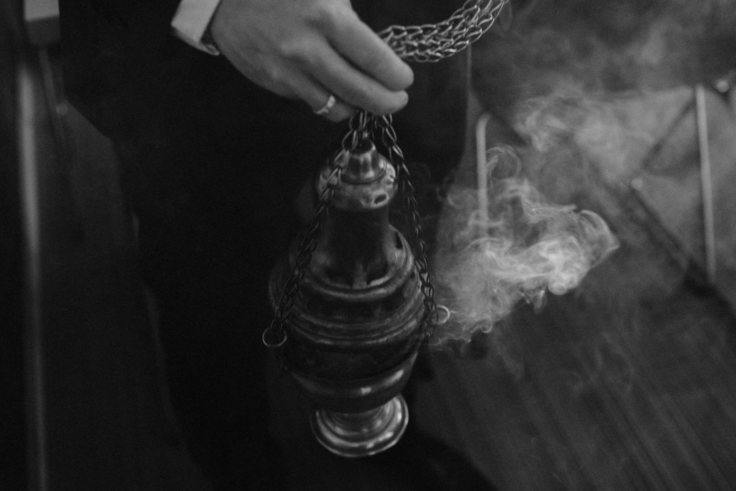 A person holding a thurible, a metal censer with chains, used in religious ceremonies. Smoke is emanating from the open top of the censer.