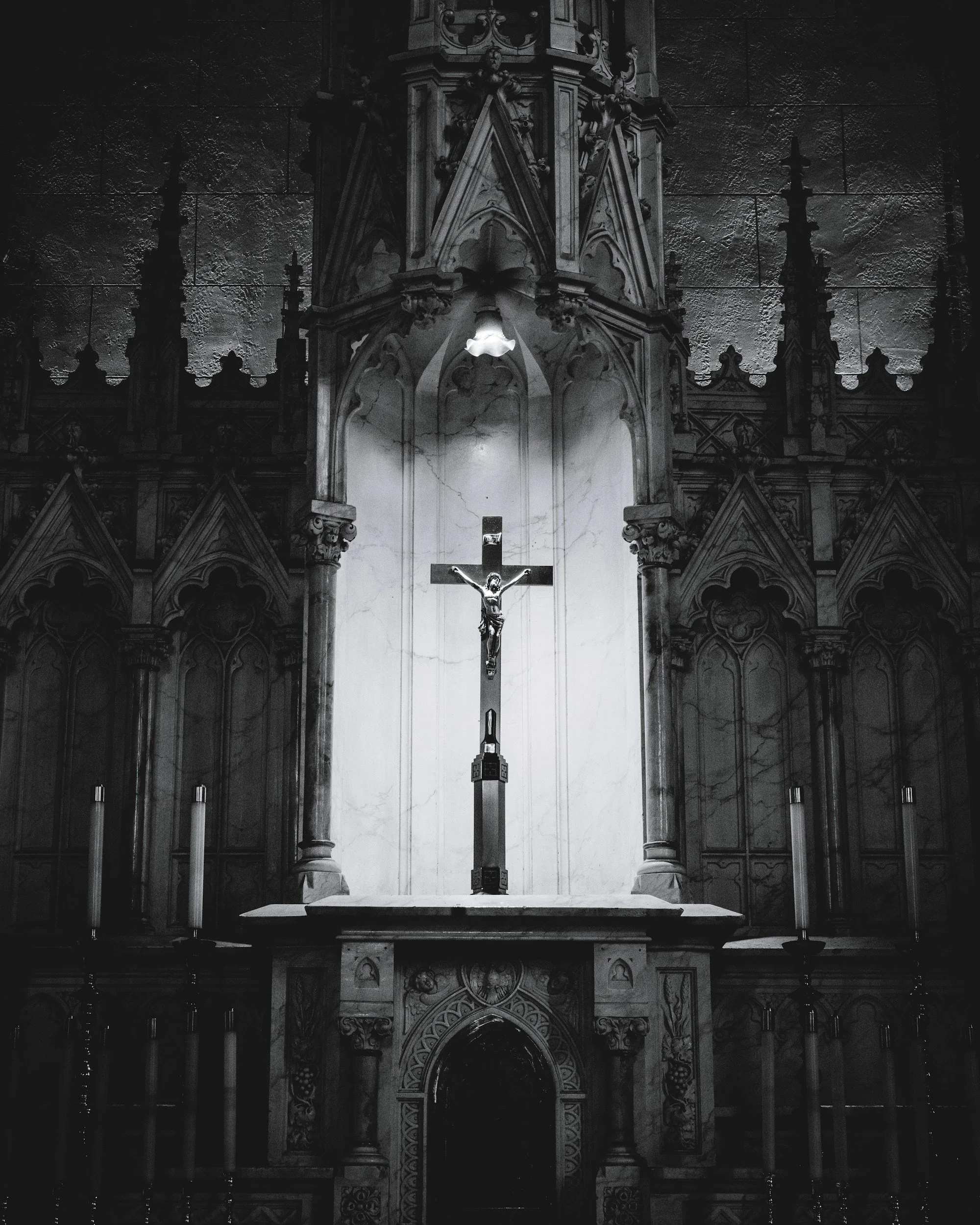 A crucifix with Jesus mounted on it, placed on an altar in a Gothic-style church, illuminated by a light above, with ornate architectural details in the background.