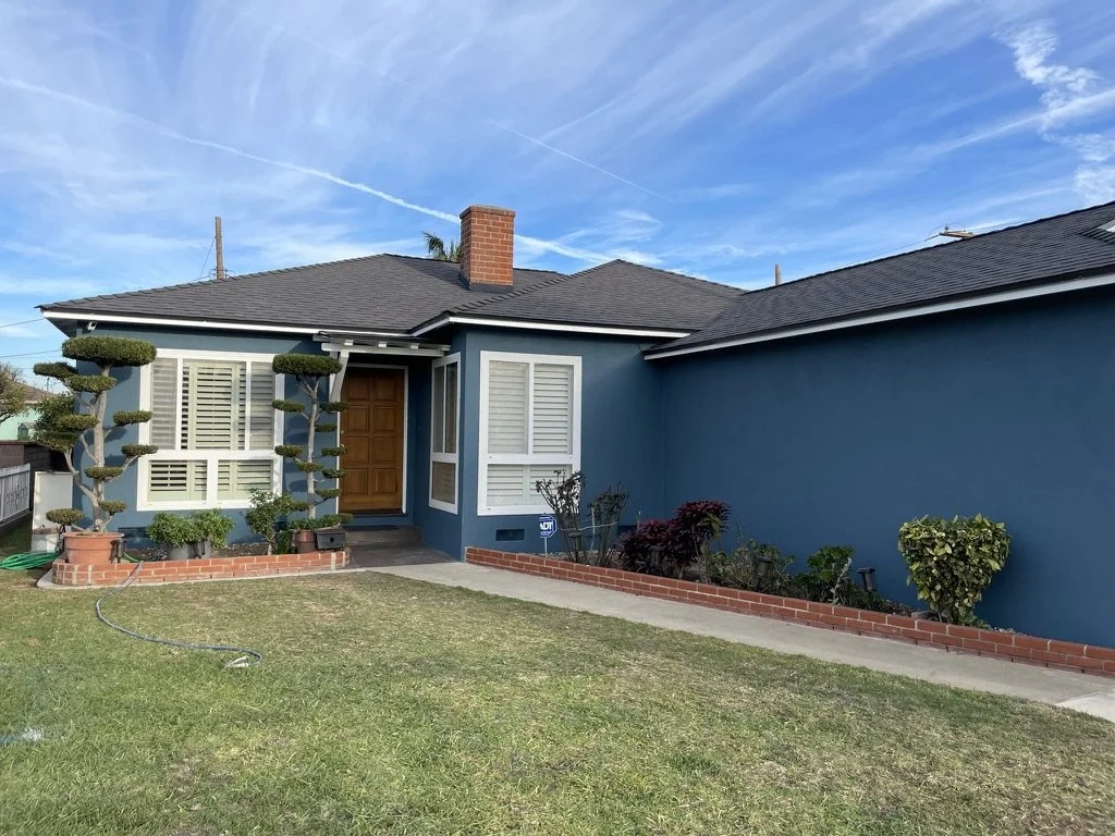 Blue house with white trim, manicured topiary trees, brick planters, and lawn.