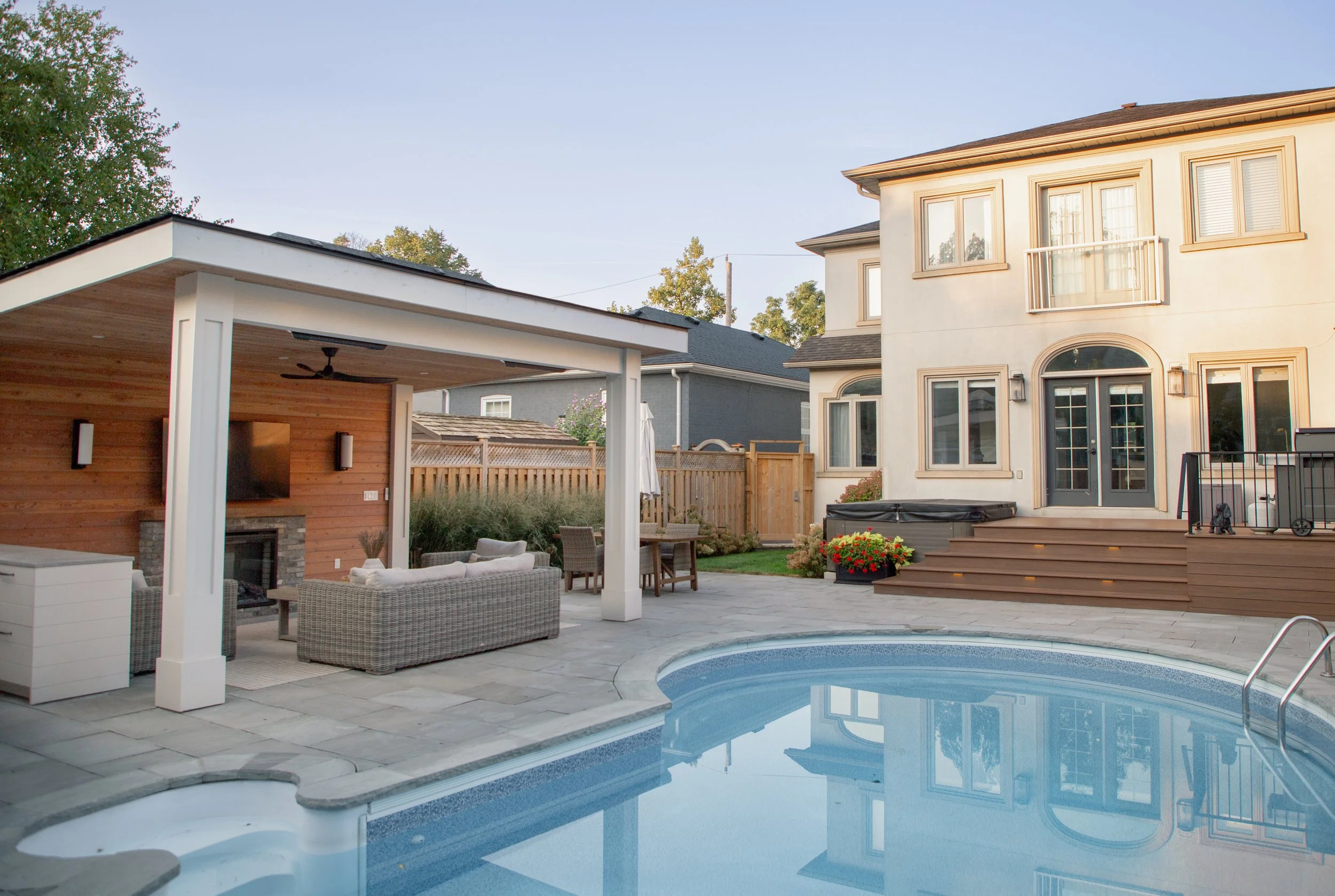 Backyard with a swimming pool, outdoor seating area, and a two-story house with beige walls and multiple windows at sunset.