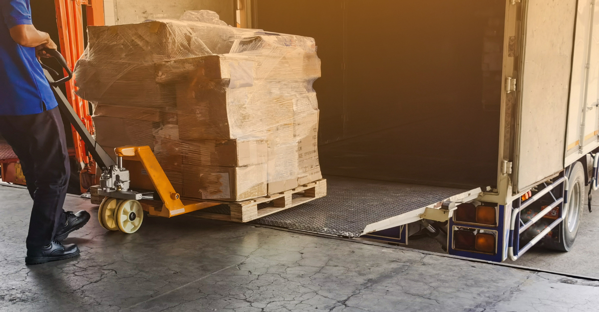 Worker loading pallets with boxes into a truck using a pallet jack