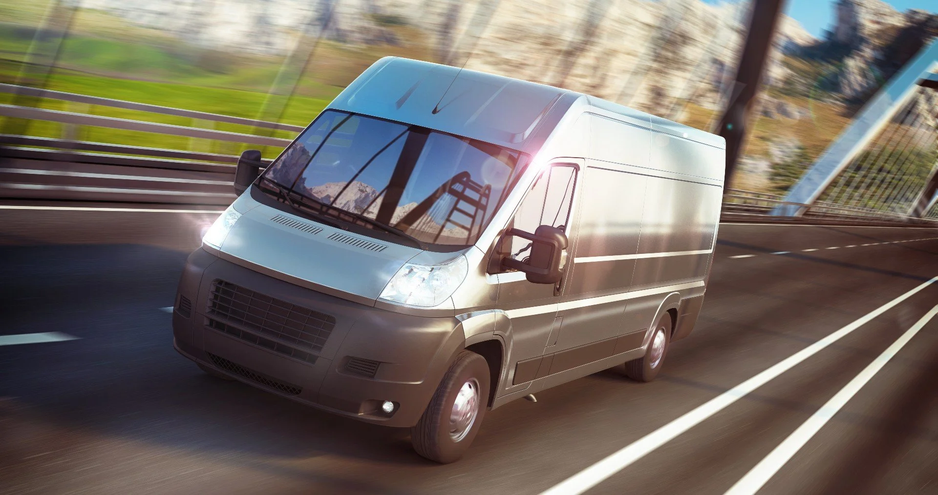 Silver cargo van driving on a highway bridge with blurred background