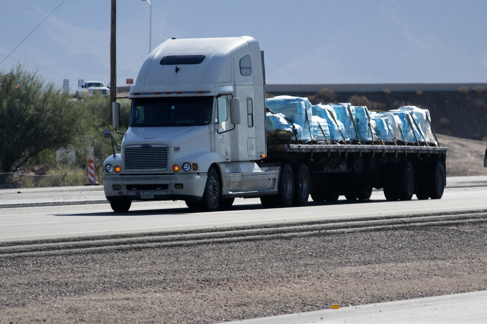 Flatbed truck transporting blue tarped cargo on a highway.