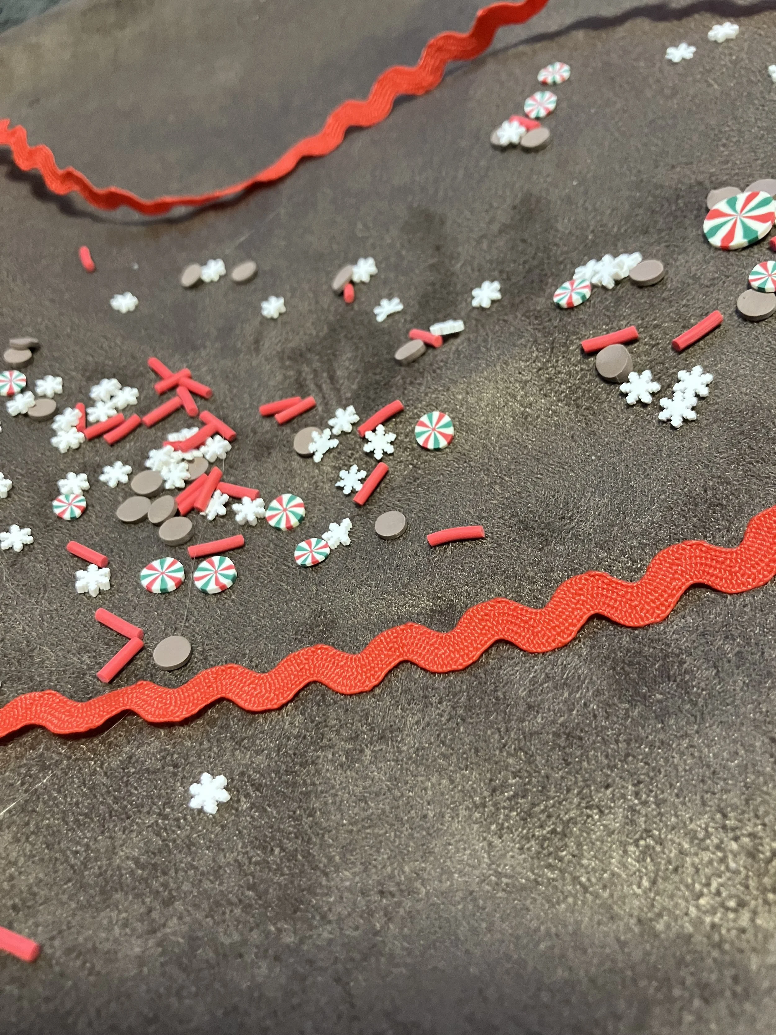 Decorative table with red ribbon border, scattered small holiday-themed confetti, and sprinkles in red, white, green, and gray colors.